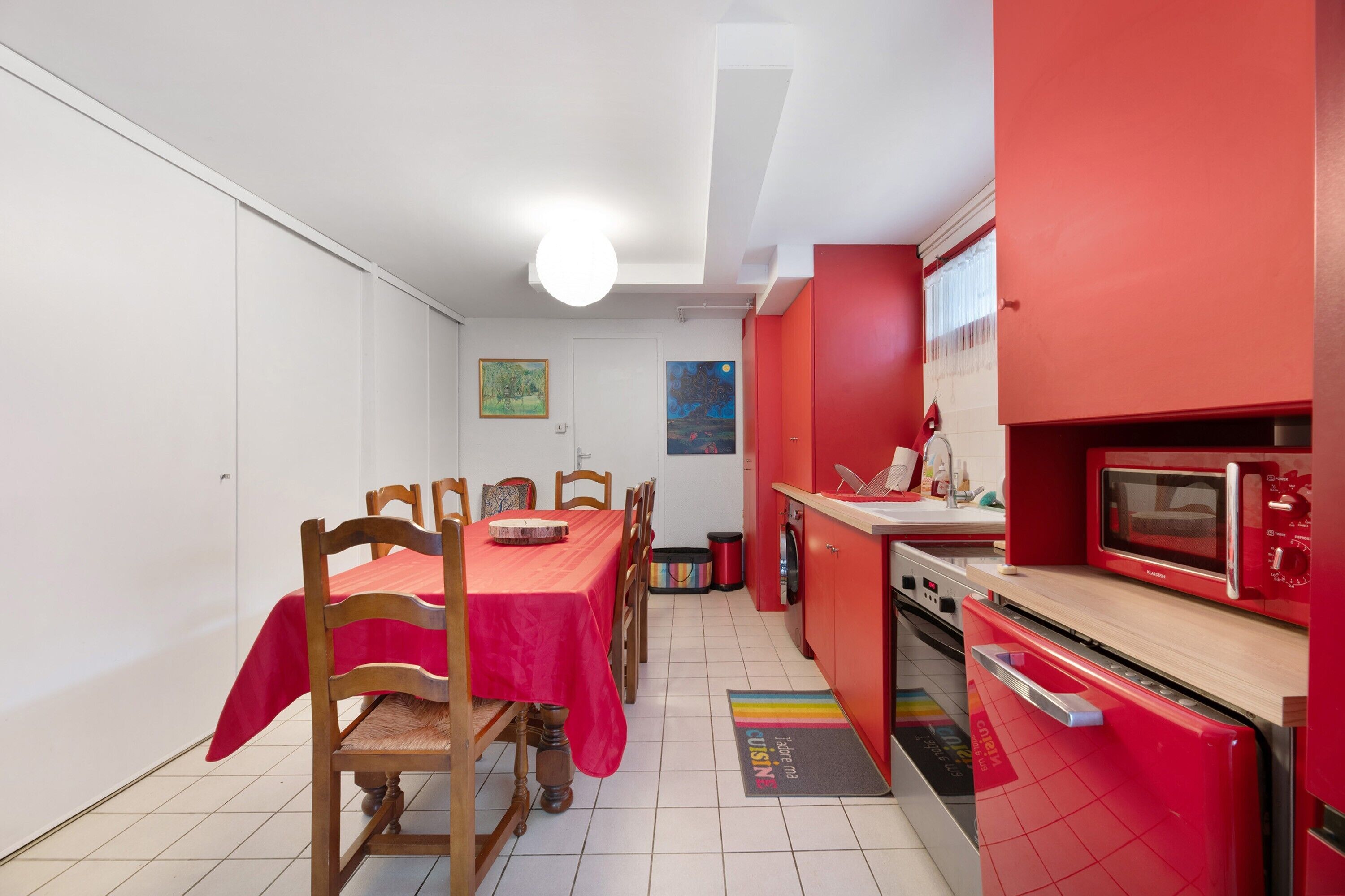 Een kleine keuken met rode apparaten, een eettafel met stoelen en een gezellig hoekje om te eten.