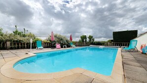 A swimming pool with a curved edge, surrounded by a stone patio, and a hedge in the background.