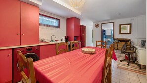 A compact kitchen with red cabinets, a washing machine, and a dining area with a red tablecloth.