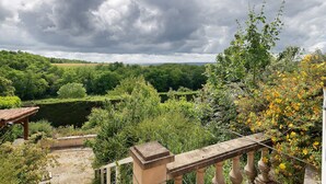 A garden with a stone balustrade, lush greenery, and a view of a distant field.