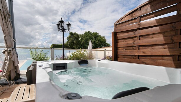 A hot tub with a view of the pool and trees, a wooden fence, and a lamp post.