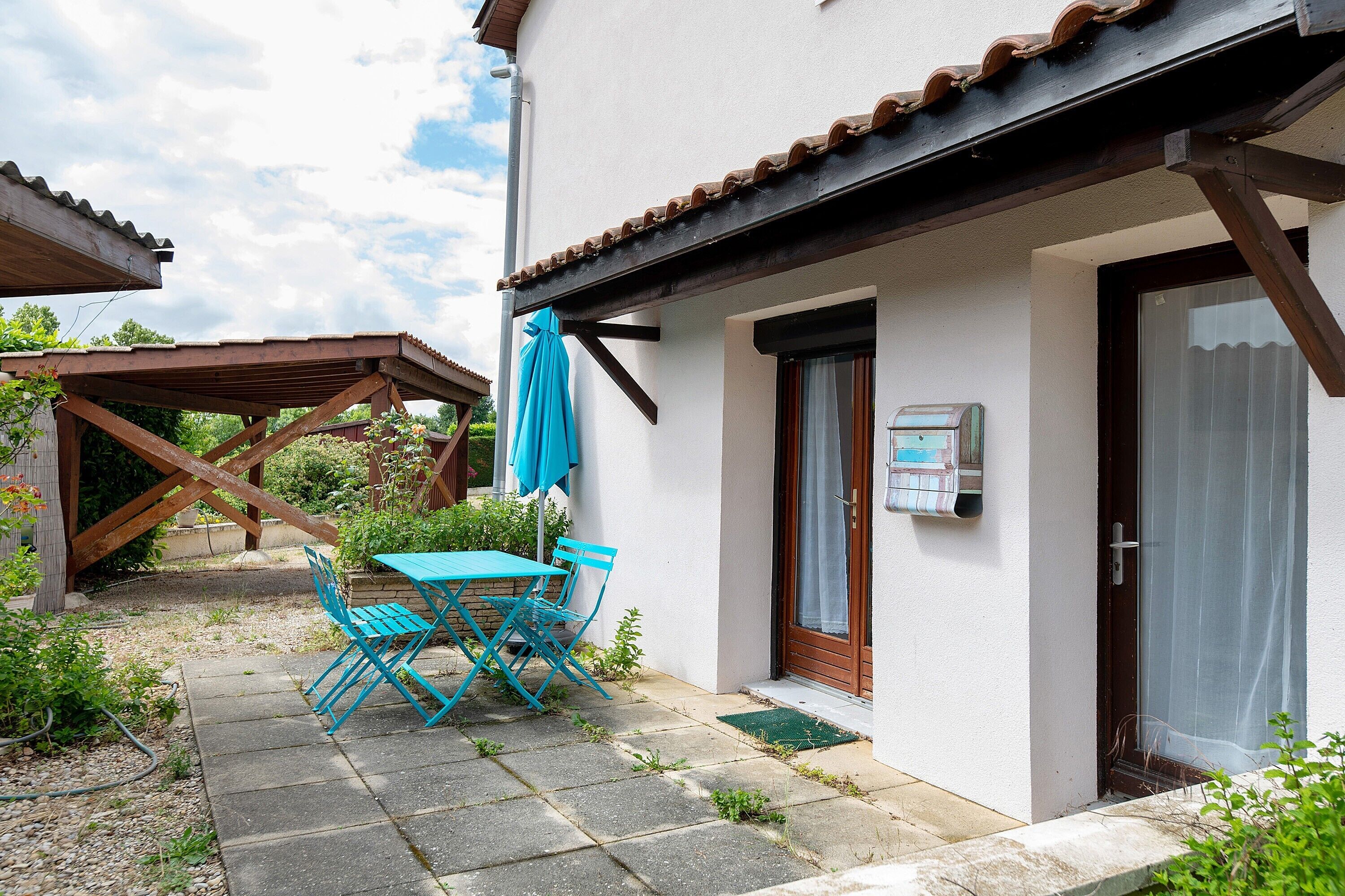 A house with a patio, a table with chairs, a blue umbrella, and a door with a window.