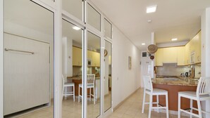 A modern kitchen with white cabinets, a central island with seating, and a sliding glass door leading to a dining area. - Vacation Studio 'Primera Linea' with Sea View, Balcony and Wi-Fi (Las Palmas de Gran Canaria)