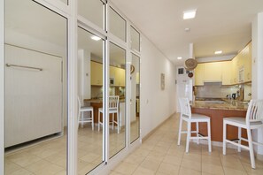 Une cuisine moderne avec des meubles blancs, un îlot central doté de sièges et une porte-fenêtre coulissante donnant sur un coin repas.