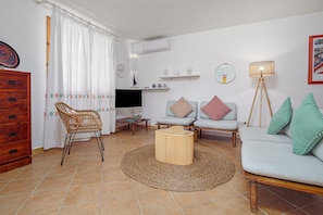 Un salon comprenant un canapé, un fauteuil, une table basse, un téléviseur et une lampe.