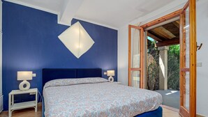 A bedroom with a bed, two bedside tables with lamps, a large window, and a view of greenery outside. - Holiday Home 'Casa Con Giardino' with Sea View, Wi-Fi and Air Conditioning (Porto Rotondo)