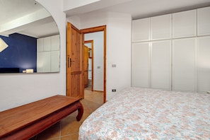 Une chambre à coucher avec un lit, un banc en bois, une armoire et un miroir.
