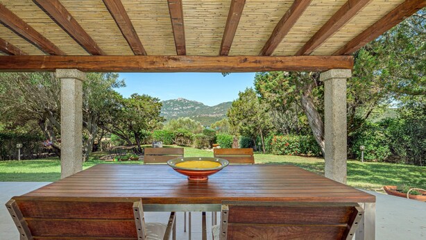 A covered outdoor dining area with a table and benches, surrounded by greenery and a view of hills. - Holiday Home 'Casa Con Giardino' with Sea View, Wi-Fi and Air Conditioning (Porto Rotondo)