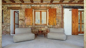A stone-walled room with two beige sofas, a small table, and wooden shutters. - Holiday Home 'Casa Con Giardino' with Sea View, Wi-Fi and Air Conditioning (Porto Rotondo)