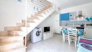 A compact kitchen with a washing machine, a dining area with a table and chairs, and a staircase. - Holiday Home 'Romantica Casa Al Mare' with Shared Pool, Wi-Fi and Air Conditioning (Viddalba)