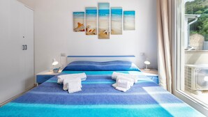 A bedroom with a bed, two bedside tables, a wall-mounted artwork, and a window with curtains. - Holiday Home 'Romantica Casa Al Mare' with Shared Pool, Wi-Fi and Air Conditioning (Viddalba)