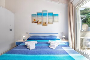A bedroom with a bed, two bedside tables, a wall-mounted artwork, and a window with curtains.