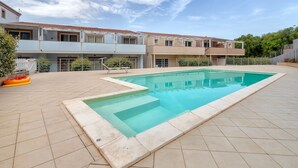 A rectangular swimming pool with a tiled deck, surrounded by a residential building with a red-tiled roof. - Holiday Home 'Romantica Casa Al Mare' with Shared Pool, Wi-Fi and Air Conditioning (Viddalba)
