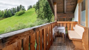 A wooden balcony with a table and bench, overlooking a green hillside.