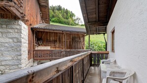 Un balcón de madera con un muro de piedra, barandilla de madera y una mesa con sillas.