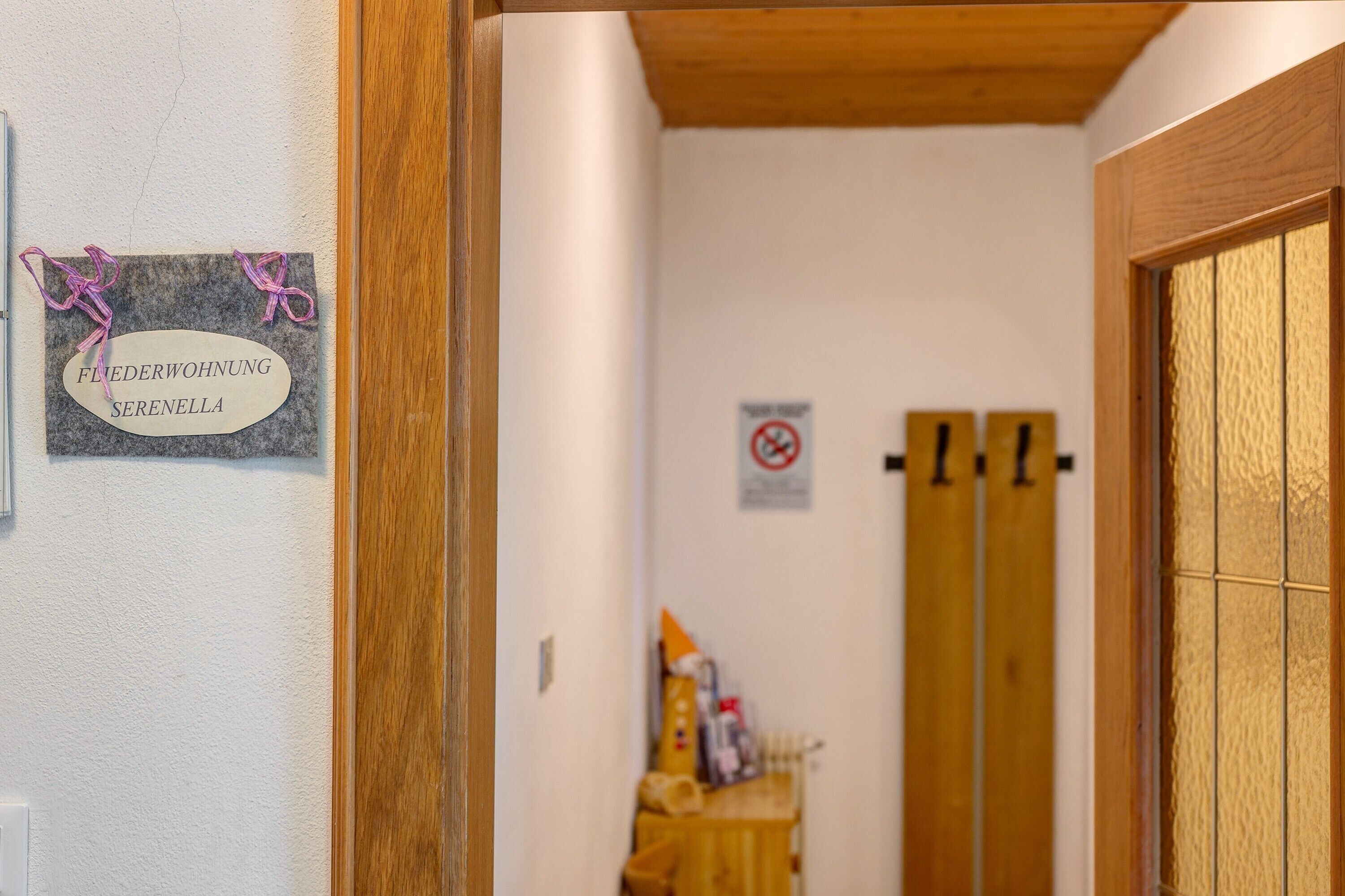 Un couloir avec une pancarte indiquant « FLEDERWOHNUNG SERENELLA », un panneau « défense de fumer » et une porte en bois.