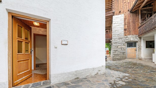 Ein mit Pflastersteinen belegter Innenhof mit einer Holztür und einer weißen Mauer.