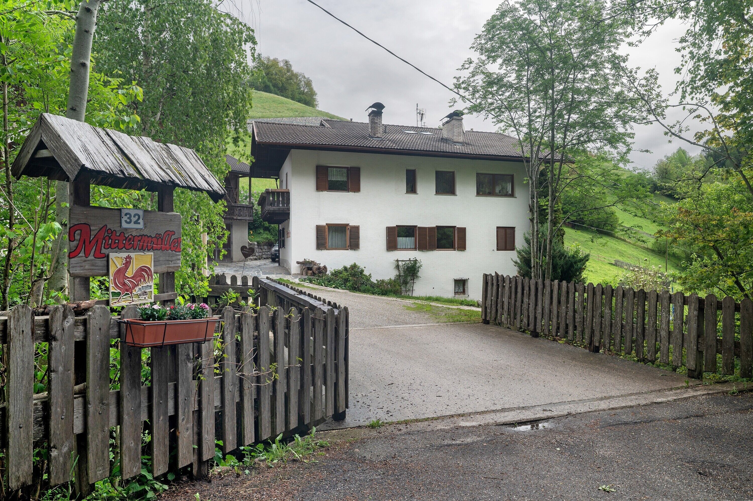 A white building with a sign reading '32 Mittermiller,' a wooden fence, and a paved driveway.