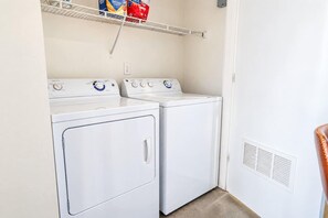 A laundry room with two white front-loading washers and dryers, a shelf above with laundry supplies, and a vent on the right wall. - CDT PHX Apt Balcony Gym Pool WD & Parking (Phoenix)