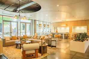 A spacious lounge area with a sofa set, coffee table, and chairs, a kitchen area with a bar, and large windows allowing natural light. - CDT PHX Apt Balcony Gym Pool WD & Parking (Phoenix)