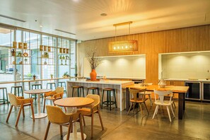 A modern restaurant with a bar area, wooden tables and chairs, and a large window offering a view of the street.
