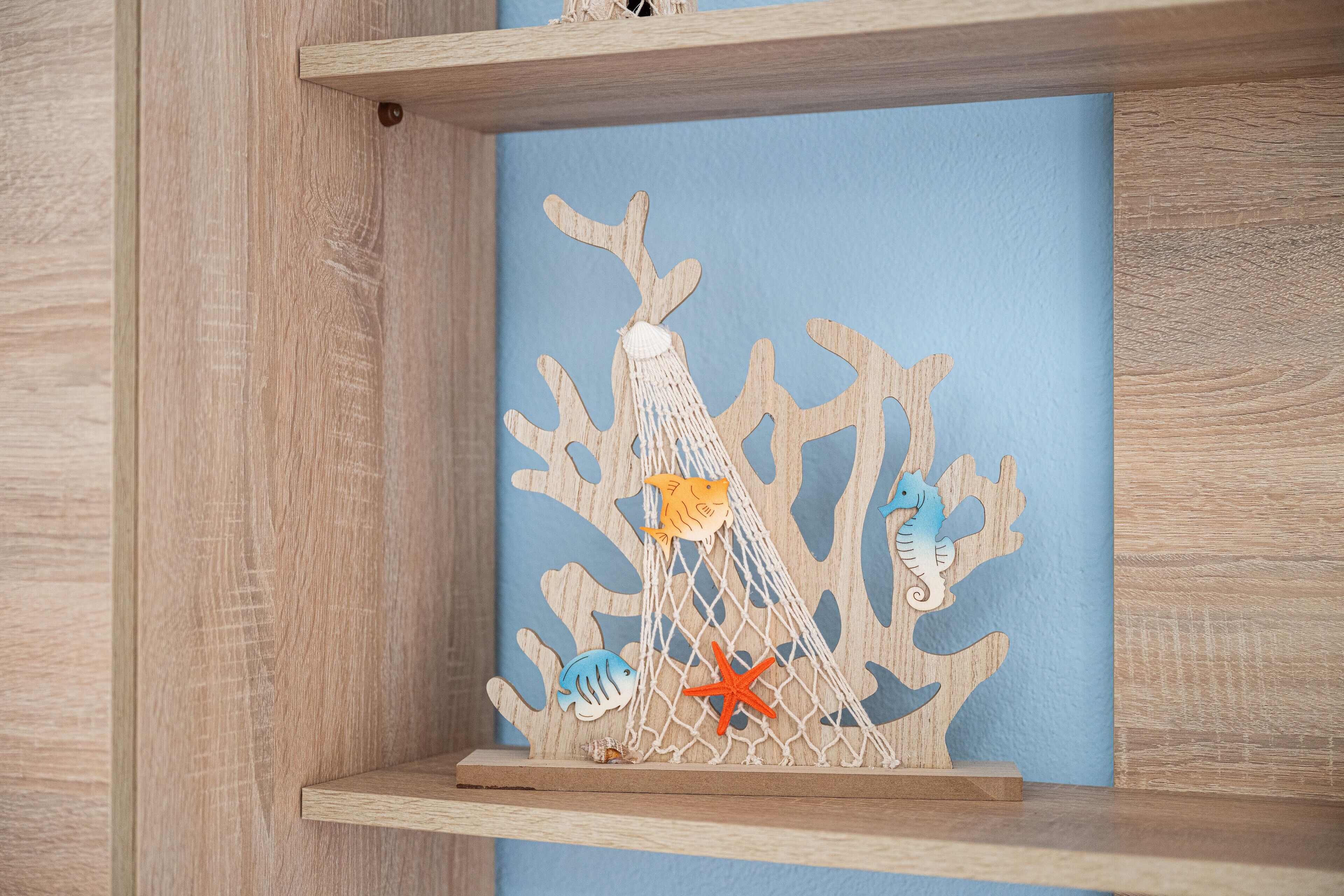 Une étagère en bois ornée d’un élément décoratif représentant un filet, des poissons et des étoiles de mer.