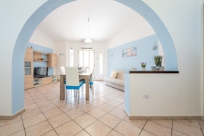 A spacious living area with a dining table, chairs, a sofa, and a kitchen area with cabinets and a TV.