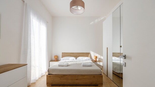 Une chambre moderne avec un lit en bois, des tables de chevet, un miroir et un luminaire au plafond.