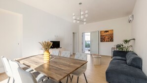 Un espace de vie moderne avec une table à manger en bois, des chaises blanches, un canapé gris et un téléviseur en arrière-plan.