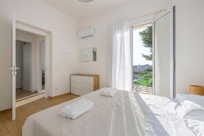 Ein Schlafzimmer mit Bett, Kommode, Klimaanlage, Spiegel und Blick durch eine Schiebetür.