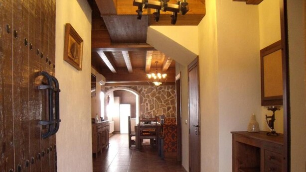 Un pasillo con puerta de madera, pared de piedra y una zona de comedor con mesa y sillas.