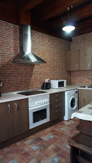 Eine Küche mit Backsteinwand, einer Edelstahl-Dunstabzugshaube, einer Mikrowelle, einem Toaster, einer Waschmaschine und Holzschränken.