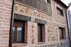 Ein Gebäude mit einer steinernen Fassade, mehreren Fenstern mit Fensterläden und einer sichtbaren Backsteinmauer.
