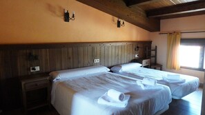 Ein Zimmer mit zwei Betten, einem Holzkopfteil, Nachttischen und einem Fenster mit Vorhängen.