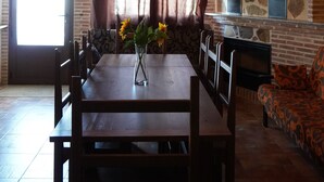 Un comedor con una mesa y sillas de madera, una araña, una pared de piedra y un ventanal con cortinas.
