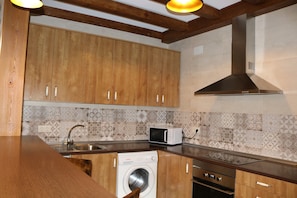 A kitchen with wooden cabinets, a washing machine, a microwave, a stove, and a ventilation hood. - Holiday Home 'La Cerecera' with Private Terrace, Wi-Fi and Air Conditioning (Los Navalucillos)