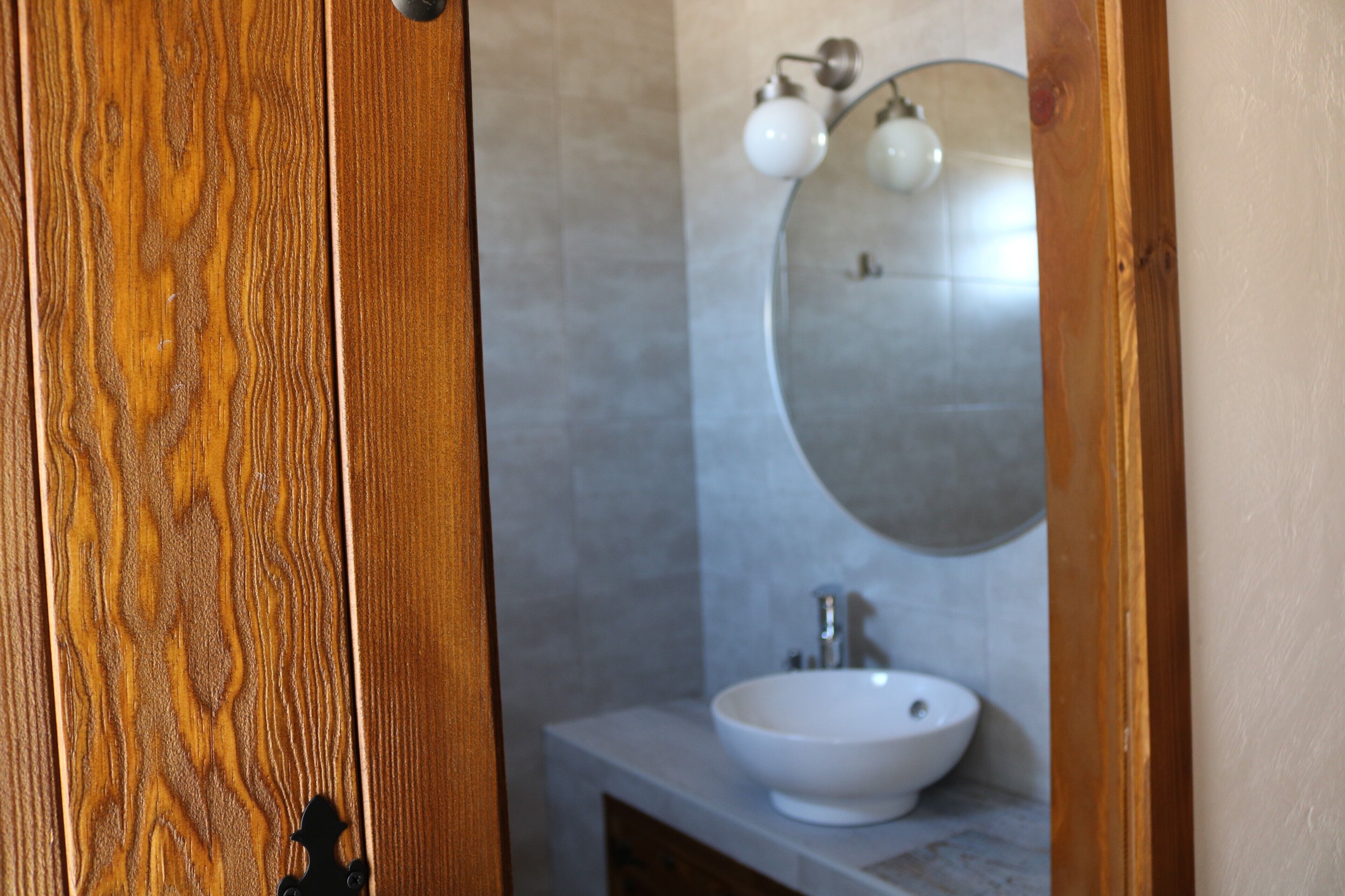 A bathroom with a wooden door, a white sink, and a mirror with two wall-mounted lights.