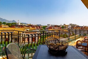 A terrace with a view of a cityscape, including buildings with red-tiled roofs and a mountain in the background. - Oikia Naxos Apartment (Giardini Naxos)