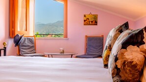 Une chambre avec une grande fenêtre, un lit, une chaise, une petite table et un tableau accroché au mur.