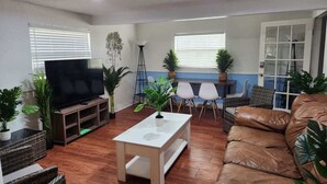 A living room with a TV on a wooden stand, a white coffee table, a brown leather sofa, and several chairs.