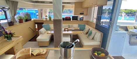 A yacht interior with a dining area, seating, a coffee machine, and a view of the sea.