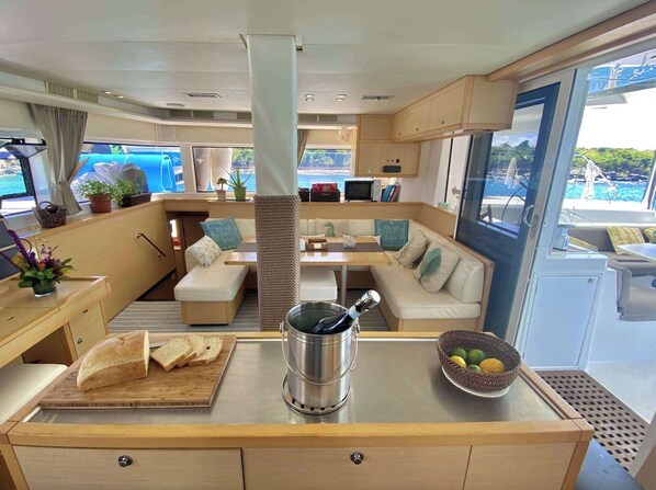 A yacht interior with a dining area, seating, a coffee machine, and a view of the sea.