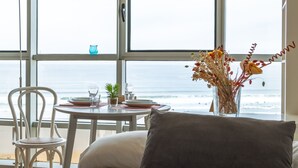 Une pièce avec vue sur l’océan, une table à manger avec des assiettes et des verres, un vase rempli de fleurs et un canapé avec un coussin.