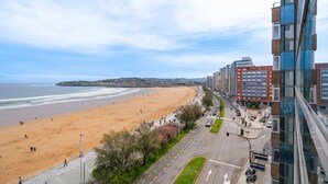 Un paysage urbain côtier avec une plage, une route bordée de voitures et des bâtiments modernes.