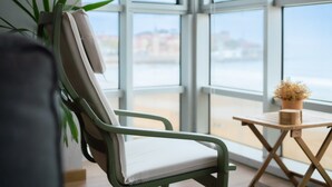 Une chaise avec un coussin, une petite table sur laquelle est posée une plante en pot, et une vue dégagée grâce à de grandes fenêtres.