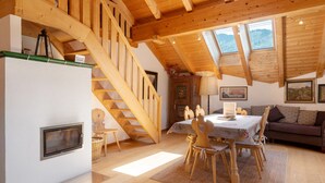 A wooden staircase, a dining area with a table and chairs, and a sofa in a room with wooden beams and skylights.