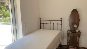Un dormitorio con cama, mesita de noche con lámpara y vista por la ventana.