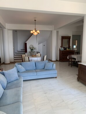 A spacious living area with a light blue sofa, a dining table with chairs, and a staircase leading to an upper floor.