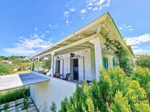A white building with a covered porch, two open doors, and a small garden area. - Villa 'Jolie  Proche Des Plages' with Sea View, Wi-Fi and Air Conditioning (Kosta)