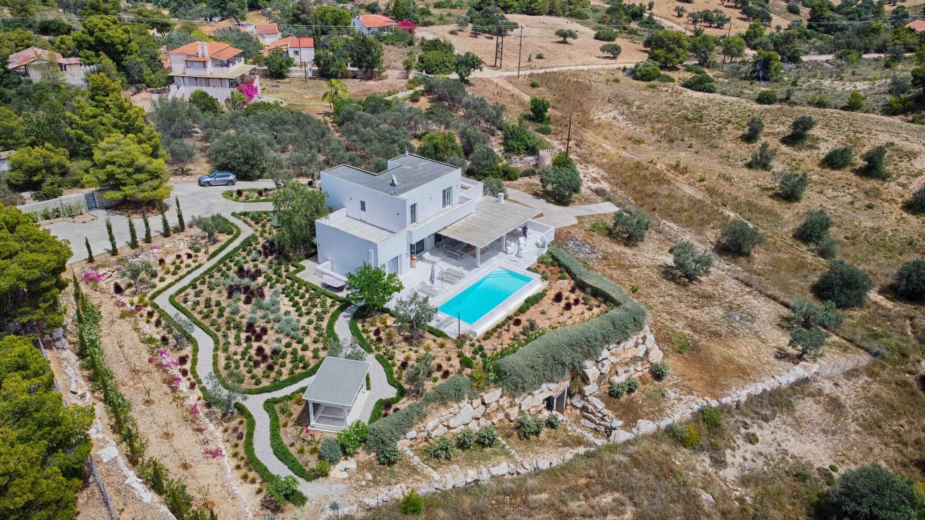 Een moderne villa met een zwembad, omgeven door aangelegde tuinen en een glooiend landschap.